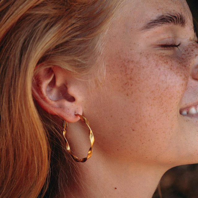 PURELEI Ke Kai Ohrringe aus 18K Gold mit leicht verdrehter Creolenform, warm und elegant am Ohr getragen.