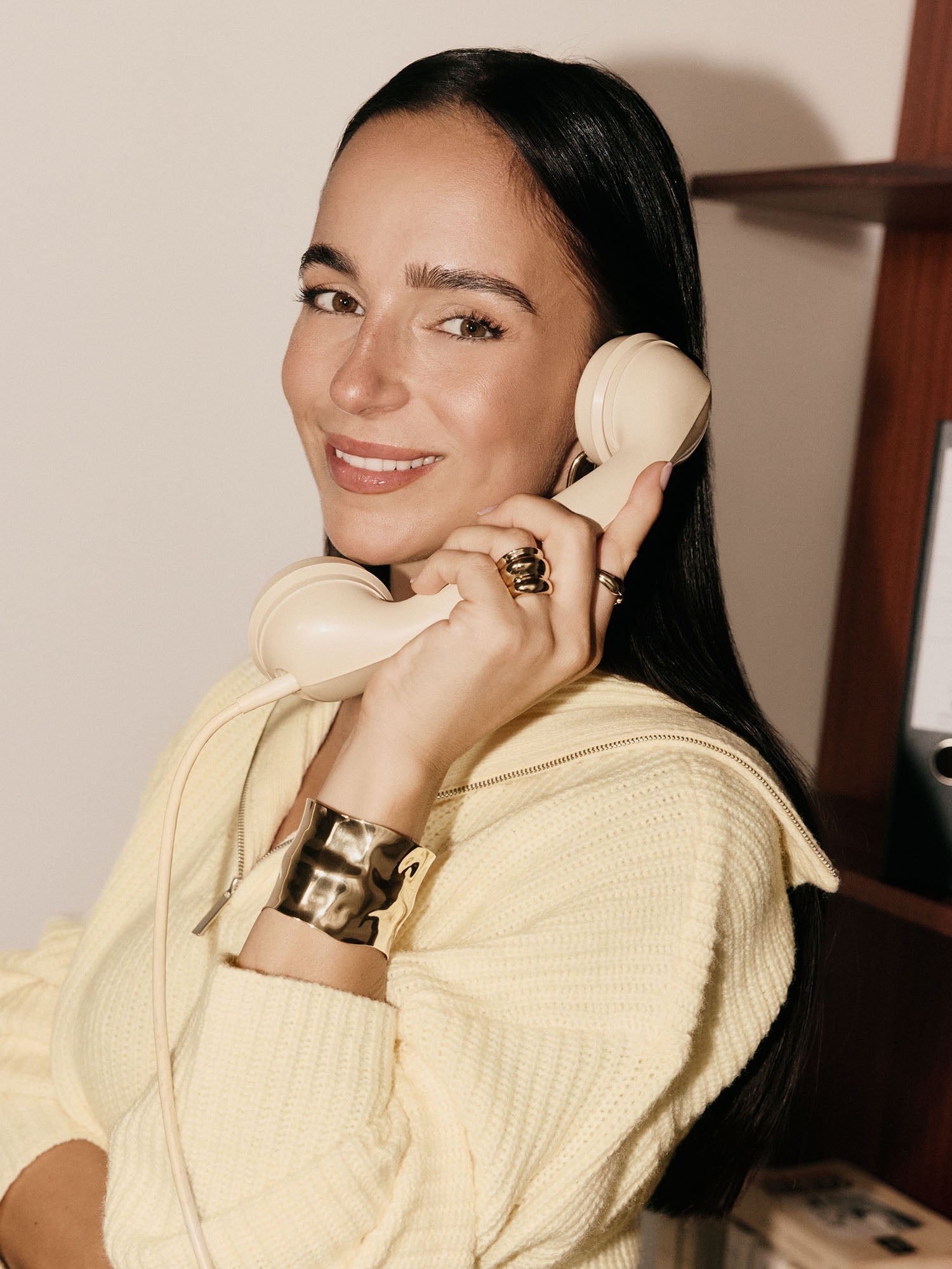 Elegantes, goldenes Armband von PURELEI, getragen mit einem Vintage-Telefon in sanften Tönen.