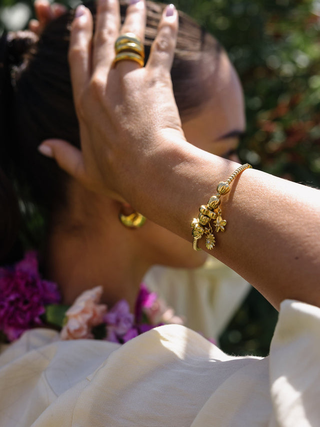 PURELEI Lei Hibiskus Charm in goldfarbenem Edelstahl mit floralem Anhänger, getragen bei sonnigem Outdoor-Licht.