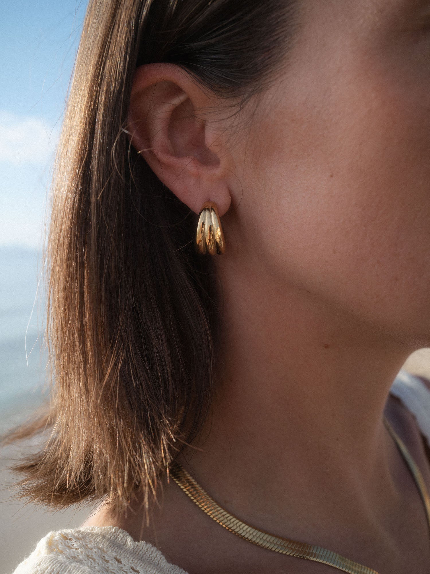 Fused Ohrringe von PURELEI, goldene Creolen-Dreier-Optik, elegant getragen am Ohr im natürlichen Tageslicht.