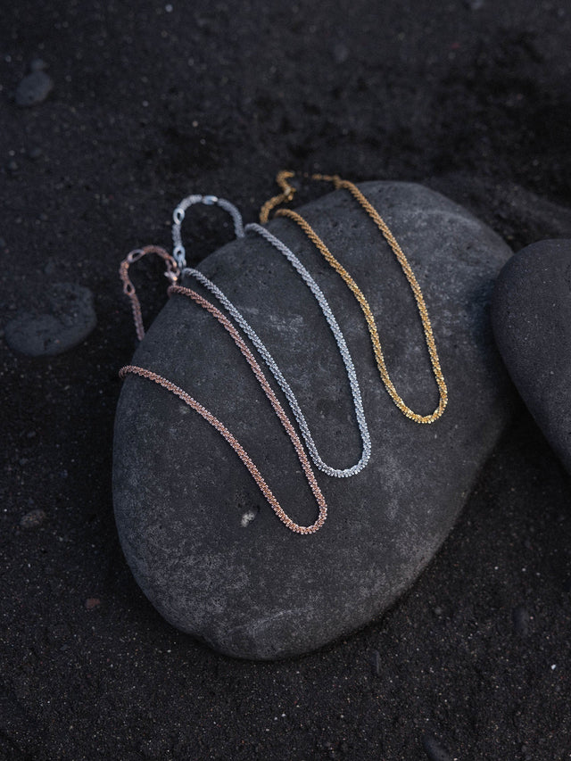 Dreifache PURELEI Lava Kette in Gold, Silber und Roségold mit gedrehter Struktur auf dunklem Lavastein.